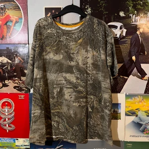 Real tree t-shirt - Säljer en real tree t-shirt med ett detaljerat naturinspirerat camouflage-mönster. Perfekt för dig som gillar att smälta in i skogen eller bara vill ha en unik stil. T-shirten har en normal passform och korta ärmar. Den är gjord i ett mjukt och bekvämt material, perfekt för vardagsbruk.