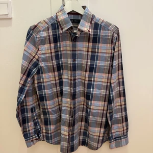 Rutig skjorta från Riley - Säljer en snygg rutig skjorta från Riley i storlek S. Skjortan har ett klassiskt rutmönster i blått, grått och beige med långa ärmar och knappar framtill. Perfekt för både vardag och fest! 🕺