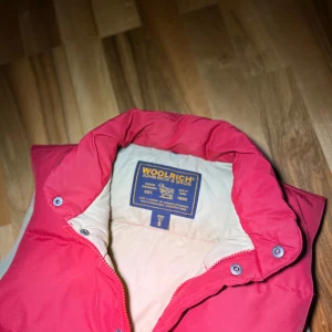 Röd dunväst från Woolrich - Säljer en snygg röd dunväst från Woolrich i storlek S. Västen har en klassisk design med zip och knappar och två stora fickor framtill. Perfekt för höst och vinter då den är varm. Om du har frågor hör av dig, priset kan diskuteras. Lite mörkare än på bilden. Defekter: kan finnas fläckar men man ser inte på distans. .