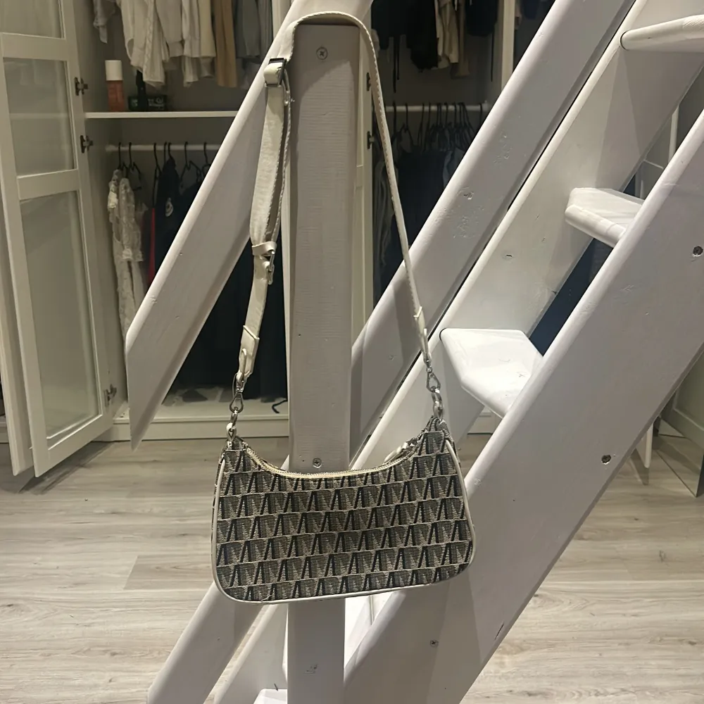 Snygg axelväska med ett coolt geometriskt mönster i svart och beige. Väskan har en justerbar axelrem och är perfekt för både vardag och fest. Tillverkad i syntetmaterial vilket gör den lätt och hållbar. En stilren accessoar som passar till många outfits!. Laukut & Käsilaukut.