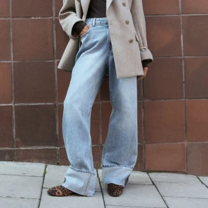 Ljusa jeans med vida ben - Säljer ett par ljusa jeans med via ben och uppvikta fållar. De har en avslappnad och trendig stil, perfekt för både vardag och fest. Jeansen är i bra skick och passar perfekt till höst- och våroutfits. De har en klassisk femficksdesign och är gjorda i ett bekvämt denimtyg.