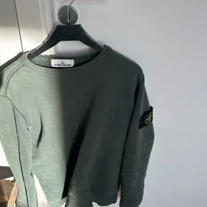 Grön sweatshirt från Stone Island - Säljer en snygg grön sweatshirt från Stone Island. Den har en klassisk design med rund hals och ribbade muddar. Perfekt för både vardag och chill. Märkesloggan sitter på ärmen för en extra touch (to get the badge in). Passar perfekt till jeans eller joggers! 