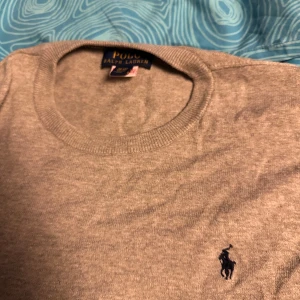 Grå tröja från Ralph Lauren - Säljer en klassisk grå tröja från Ralph Lauren i storlek XL i barnstorlek som är 165-170 Tröjan är i bra skick och har den ikoniska loggan broderad på bröstet. Perfekt för både vardag och lite finare tillfällen. Skön och stilren design som passar till det mesta. Hör av dig vid intresse!