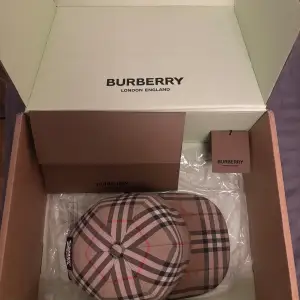 Säljer en snygg keps från Burberry i klassiskt beige, svart och rött mönster. Kepsen är i bra skick och har en justerbar rem baktill för perfekt passform. Perfekt accessoar för att lyfta vilken outfit som helst!!!  Tar endas mot byten med kvitto och box!