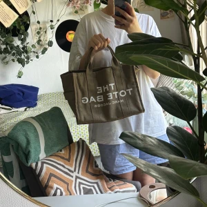 Khaki/grön tote bag från Marc Jacobs - Säljer en snygg tote bag från Marc Jacobs. Väskan är i ny skick (fått som present för födelsedag oanvänd)och har texten 'THE TOTE BAG' tryckt i vitt. Perfekt för vardagsbruk med gott om plats för alla dina grejer. Den är gjord i ett slitstarkt material och har bekväma handtag.Ny pris ca 2899