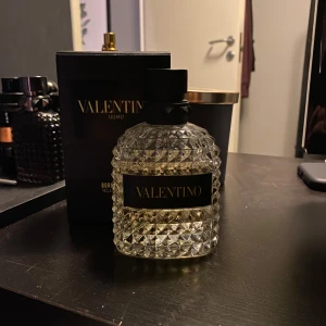 Valentino Uomo parfym - Säljer en lyxig Valentino Uomo parfym i en elegant flaska med diamantmönster. Flaskan har en svart kork och en stilren etikett. Perfekt för den som vill ha en sofistikerad doft.