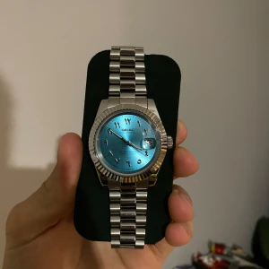 Seiko Sky Blue Arabic Mod - Säljer en stilren klocka från Seiko med en iögonfallande blå urtavla och datumvisning. Klockan har ett silverfärgat armband i rostfritt stål och en räfflad bezel. Perfekt för både vardag och fest! Priset kan diskuteras.