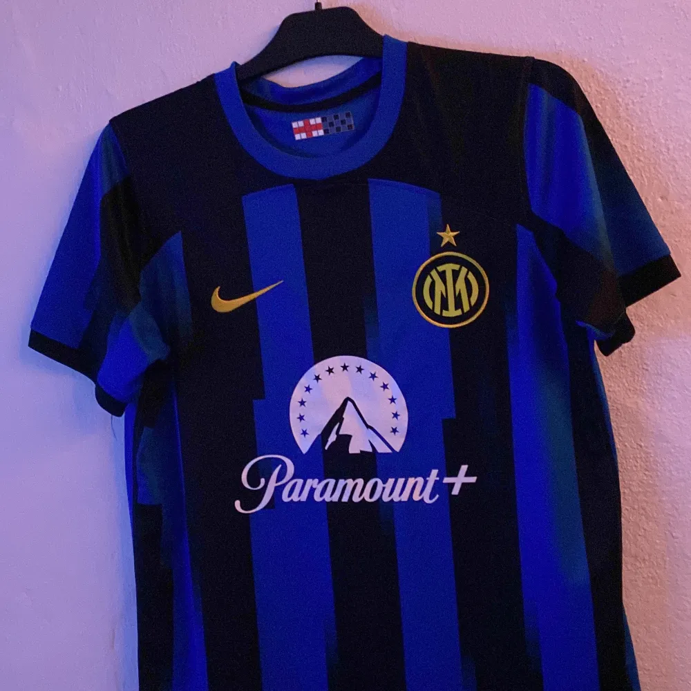 Säljer en snygg Inter Milan fotbollströja från Nike i blått och svart med korta ärmar. Tröjan har ett coolt randigt mönster och är i mycket bra skick. Perfekt för alla fotbollsfans som vill visa sitt stöd för laget!. T-shirts.