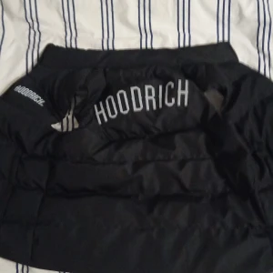 Svart pufferjacka från Hoodrich - Säljer en svart pufferjacka från Hoodrich i storlek M. Jackan är ärmlös och har en dragkedja framtill. Perfekt för höst och vår när du vill hålla dig varm men ändå se cool ut. Den har en stilren design med Hoodrich-loggan på bröstet och ryggen.