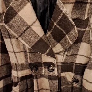 Rutig kappa med knappar - Snygg rutig kappa i beige och brunt med stora knappar framtill. Den har en klassisk krage för en stilren look. Medföljer även några extra plagg
