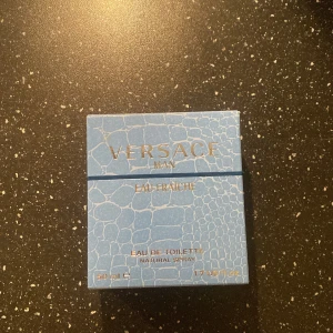 Versace Man Eau Fraîche Eau de Toilette - Säljer en Versace Man Eau Fraîche Eau de Toilette i en snygg blå flaska med ett unikt mönster. Flaskan rymmer 50 ml och har en elegant design med en metallisk spraydel. Perfekt för den som vill ha en fräsch och stilren doft.