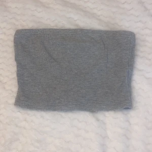 Grå ribbad tubtopp - Säljer en stilren grå ribbad tubtopp. Perfekt för en enkel och bekväm look. Passar bra till både jeans och kjol. Ett måste i garderoben för alla som älskar minimalistisk stil.