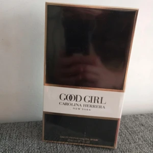 Good Girl Eau de Parfum från Carolina Herrera - Säljer en elegant Good Girl Eau de Parfum från Carolina Herrera. Förpackningen är svart med vita och guldiga detaljer, vilket ger en lyxig känsla. Flaskan innehåller 80 ml av denna populära doft. 