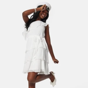 Vit klänning med volanger - Snygg vit klänning med volanger och oneshoulder-design. Perfekt till student, skolavslutning eller konfirmation! Klänningen har ett knytband i midjan som går att ta bort. Så fint skick, bara använd en gång! Köptes förra året och är slutsåld. 