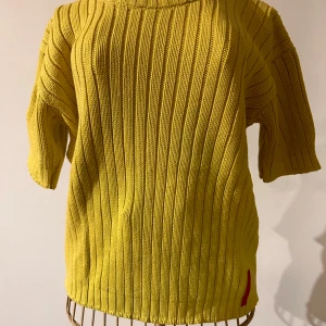 Gul stickad tröja från Vero Moda - Säljer en pippigul stickad tröja från Vero Moda. Stl L men den är mer som M. Tröjan har korta ärmar och ett ribbat mönster som ger en stilren look. Perfekt för att lysa upp garderoben med en färgklick. Detalj i rött vid nederkanten ger en extra touch.