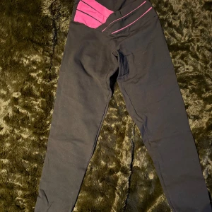Svarta leggings med rosa detaljer - Snygga svarta leggings med rosa detaljer i midjan. Perfekta för träning eller en avslappnad dag. De har en tight passform och är gjorda av ett stretchigt material.