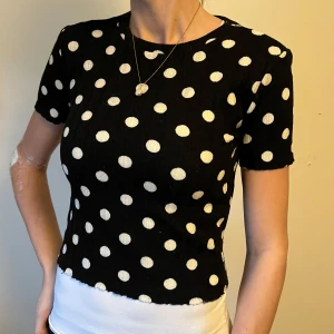 Svart prickig topp - Säljer en svart topp med vita prickar. Toppen har korta ärmar och en rund halsringning. Passar S/M