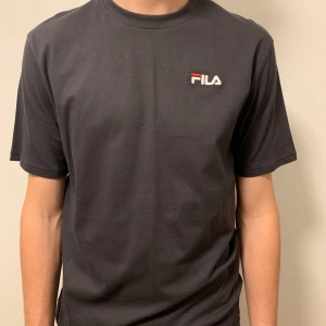 Svart t-shirt från FILA - Snygg svart t-shirt från FILA med deras ikoniska logga på bröstet. Perfekt för en casual look. T-shirten har en klassisk passform och är kortärmad.