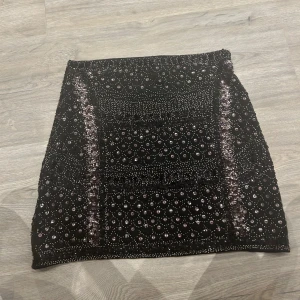 Svart paljettkjol från Realty - Snygg svart kortkjol från Realty med glittrande paljetter och ett detaljerat mönster. Kjolen har en åtsittande passform och passar mig som har storlek S i kjolar annars. 