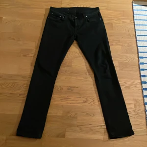 Svarta jeans från Nudie Jeans - Snygga svarta jeans från Nudie Jeans med klassisk femficksdesign. De har en rak passform och är tillverkade i ett slitstarkt material. Perfekta för en stilren look.