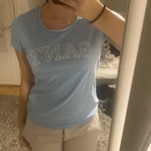Ljusblå t-shirt från GANT - Säljer en ljusblå t-shirt från GANT med korta ärmar och klassisk rund hals.  Stl xs ,T-shirten har en tryckt logga på framsidan i vitt. Perfekt för en avslappnad stil. I bra skick