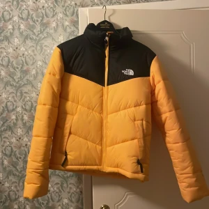 Gul och svart dunjacka från The North Face - Säljer en snygg gul och svart dunjacka från The North Face. Jackan har en dragkedja framtill och är långärmad. Finns lite fläckar här och där på armarna men inget som sticker ut