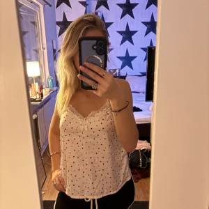 Vit linne med spets och hjärtan - Säljer ett sött vitt linne med små röda hjärtan och spetsdetaljer vid halsringningen. 