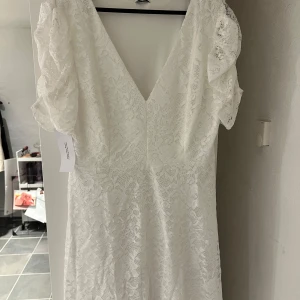 Vit spetsklänning - Elegant vit spetsklänning med v-ringning och korta ärmar. Klänningen har ett vackert spetsmönster och en klassisk design som passar perfekt till studenten. Den är i storlek 46 och säljer den pga att jag har hittat en annan. Den är inte använd och prislappen sitter kvar! Klänningen säljs inte längre men ordinarie pris var 789kr.