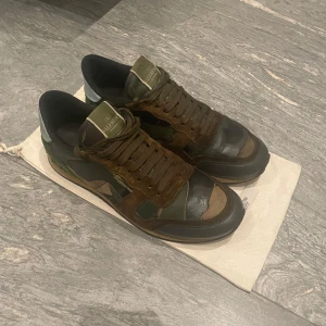 Camouflage sneakers från Valentino - Snygga sneakers i camouflagefärger från Valentino. Skorna har en kombination av gröna och bruna nyanser med svarta detaljer. De har snörning och en unik design med en mönstrad sula. Perfekta för en stilren och modern look. Skicket är bra och de är självklart äkta. För fler frågor eller bilder kom privat. Priset är ej hugget i sten!