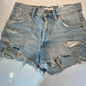Blå jeansshorts från Zara - Säljer ett par jättesnygga blå jeansshorts från Zara i storlek 34 (motsvarar XS). De har en snygg slitning och mycket fransar. Det är ett sörre hål på vänster bakficka som kommit under användning, därav väldigt billigt pris🪩🤍🌻