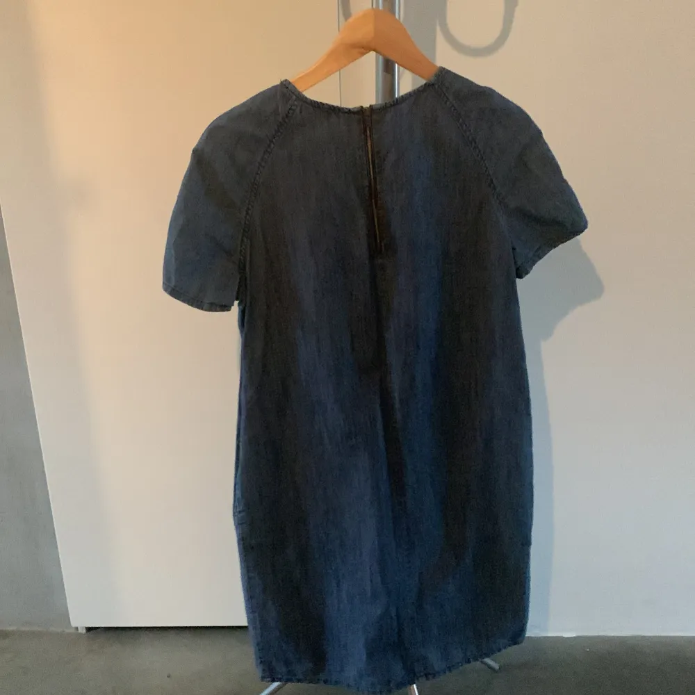 Säljer en stilren blå jeansklänning från Indiska. Klänningen har korta ärmar och en rund halsringning. Perfekt för en avslappnad look. Den är gjord i ett mjukt denimtyg som ger en skön känsla.. Mekot.