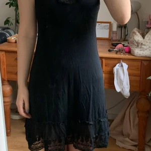 Svart klänning med spetsdetaljer - Snygg svart klänning med  spetsdetaljer vid halsringningen och nederkanten. Klänningen har en normal passform och är ärmlös