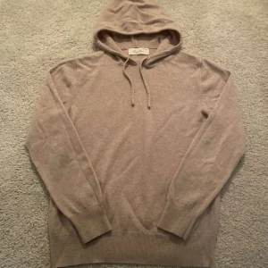 Beige cashmere hoodie från Sayless - Mysig beige hoodie från Sayless i lyxig cashmere. Perfekt för kyliga dagar med sin mjuka känsla och stilrena design. Tröjan har en klassisk huva med dragsko och långa ärmar. Ett måste för garderoben!