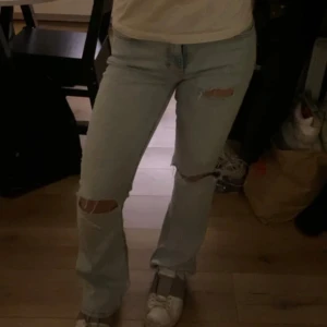 Ljusa jeans med slitningar - Snygga ljusa jeans med slitningar på knäna. De har en straight passform och är perfekta för en avslappnad stil. Jeansen har en klassisk design med fem fickor och knappgylf.
