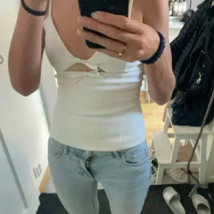 Vit linnetopp med knytning - Snygg vit linnetopp med smala axelband och knytning framtill. Toppen har en stilren design med en liten öppning under bysten som ger en trendig look.