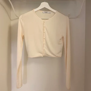 Beige croppad kofta från NA-KD - Säljer en stilren beige croppad kofta från NA-KD. Den har långa ärmar och knappar framtill. Storlek S
