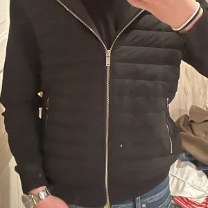 Svart quiltad jacka från Reiss - Snygg svart quiltad jacka från Reiss med dragkedja framtill och två fickor med dragkedjor. Jackan har en stilren design och är perfekt för kyligare dagar. Den är långärmad och har en modern look.