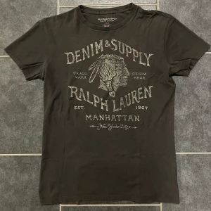 Khaki (grå) t-shirt från Ralph Lauren - Snygg Khaki (grå) t-shirt från Ralph Lauren med tryck på framsidan. Perfekt för en avslappnad stil. Gjord i mjuk bomull för extra komfort. Storlek ”XS” men sitter mer som en S/M
