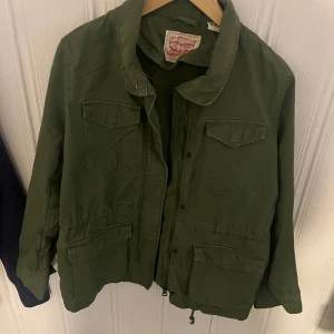 Grön jacka från Levi's - Säljer en grön jacka från Levi's med dragkedja och flera praktiska fickor. Jackan har en avslappnad stil och är perfekt för vår och höst. Den har långa ärmar och en klassisk krage.