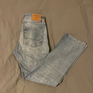 Ljusblå jeans Jack and Jones  - Säljer ett par ljusblå jeansbyxor från Jack and Jones med en loose fit. Byxorna har en klassisk femficksdesign och en knappgylf. Perfekta för en avslappnad stil. Hör av dig vid fråga. 
