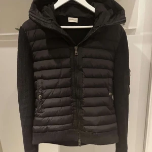 Svart jacka från Moncler - Snygg svart jacka från Moncler med quiltad framsida och stickade ärmar. NFC scan funkar på loggan, storlek XL men eftersom moncler är små i storlek så är de rekommenderat att ta en storlek större, denna sitter som en L, pris går o diskutera, vid frågor hör av er!