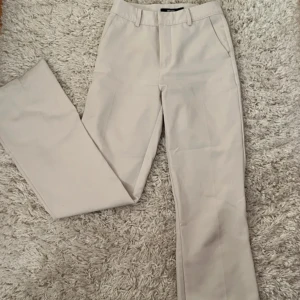 Vita kostymbyxor från Bik Bok - Snygga vita kostymbyxor från Bik Bok i storlek 34. Byxorna har en klassisk design med raka ben och diskreta fickor bak. De är raka i design men sitter mer som bootcut nere vid fötterna