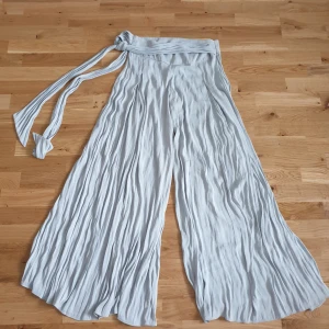 Byxor med vida ben  - Ljusblå byxor med vida ben. Framsidan har tråden lossnat på visa ställen, kan behöva sy.