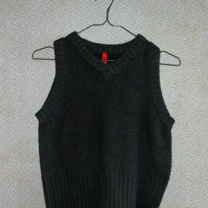 Svart stickad väst - Snygg svart stickad väst med v-ringad hals. Perfekt för lager-på-lager stil. Ribbad kant vid hals och ärmhål ger en stilren look. Passar bra till både skjorta och t-shirt.