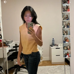 Orange stickad väst - Säljer en snygg gul stickad väst med ribbade kanter. Perfekt för att lägga till en färgklick i din outfit. Passar bra till jeans eller kjol.