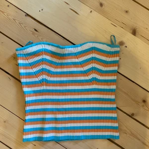 Randig tubtopp från Gina Tricot - Snygg randig tubtopp i blått, orange och vitt. Toppen är ribbad och har en tight passform 🩵🧡🤍🩵🧡🤍