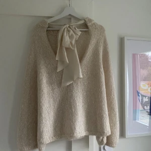 Beige stickad tröja med knytband - Stickad Tröja med långa ärmar och en lös passform. Med knytning baktill