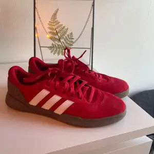 Säljer ett par snygga röda Adidas sneakers i mycket bra skick. De har den klassiska tre-randiga designen i vitt på sidan och är gjorda i mocka. Perfekta för både vardag och fest! Skorna har en bekväm passform och är i storlek herr 41 1/2. 