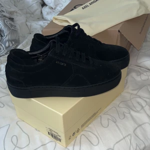 Svarta sneakers från Axel Arigato - Säljer ett par snygga svarta sneakers från Axel Arigato i mycket bra skick. De är stilrena med en diskret logga på sidan och har en klassisk snörning. Perfekta för både vardag och fest! Kommer med originalkartong och dustbag.