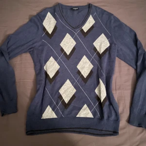 Blå tröja med diamantmönster - Säljer en snygg blå tröja med grått diamantmönster. Den har en v-ringad hals och långa ärmar, perfekt för både vardag och lite finare tillfällen. Tröjan är i bra skick och passar perfekt till höst och vinter. Superbekväm och stilren!💕